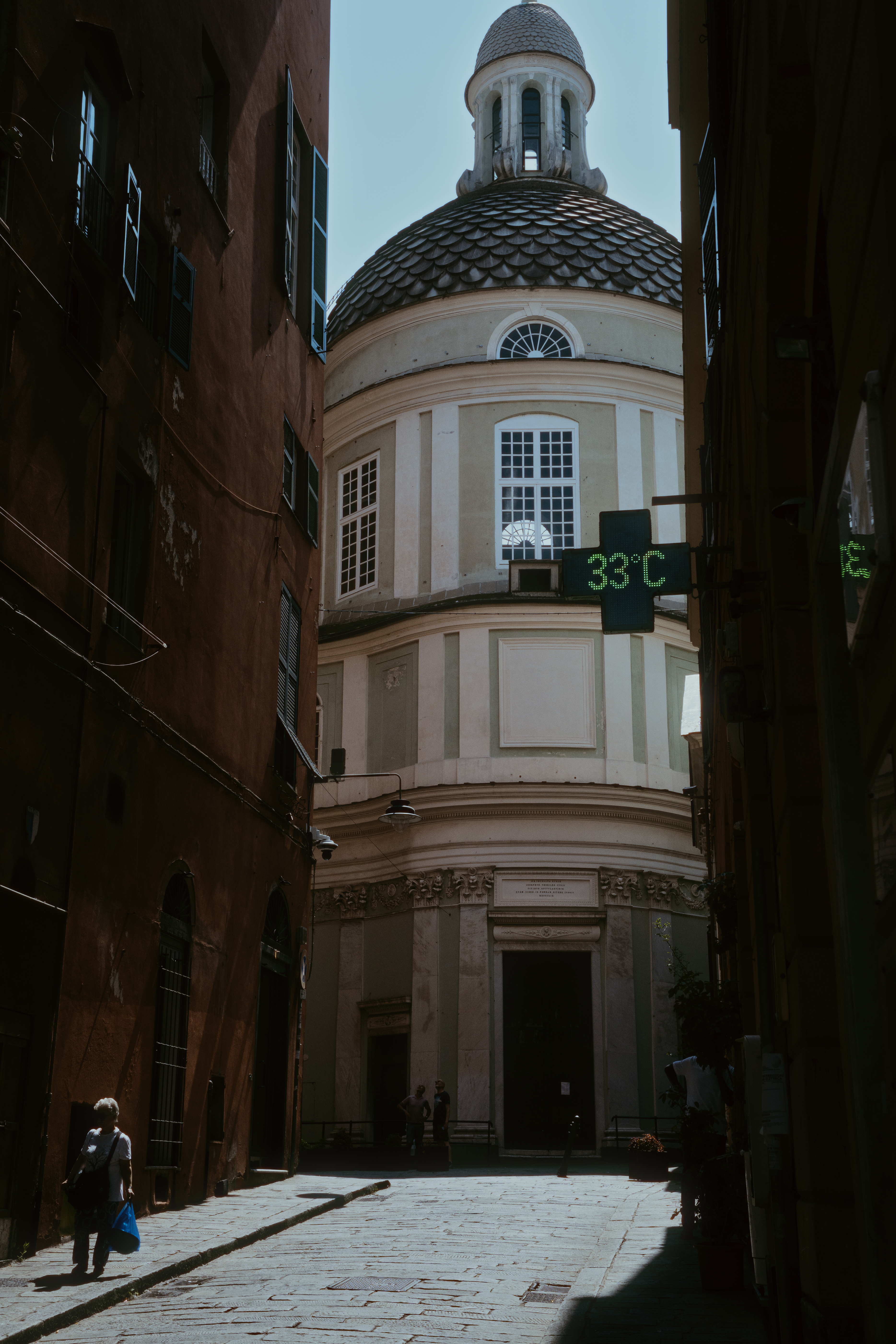 looking down an alleyway in Genoa Italy seeing a church. In the foreground a pharmacy sign reads 33ºC