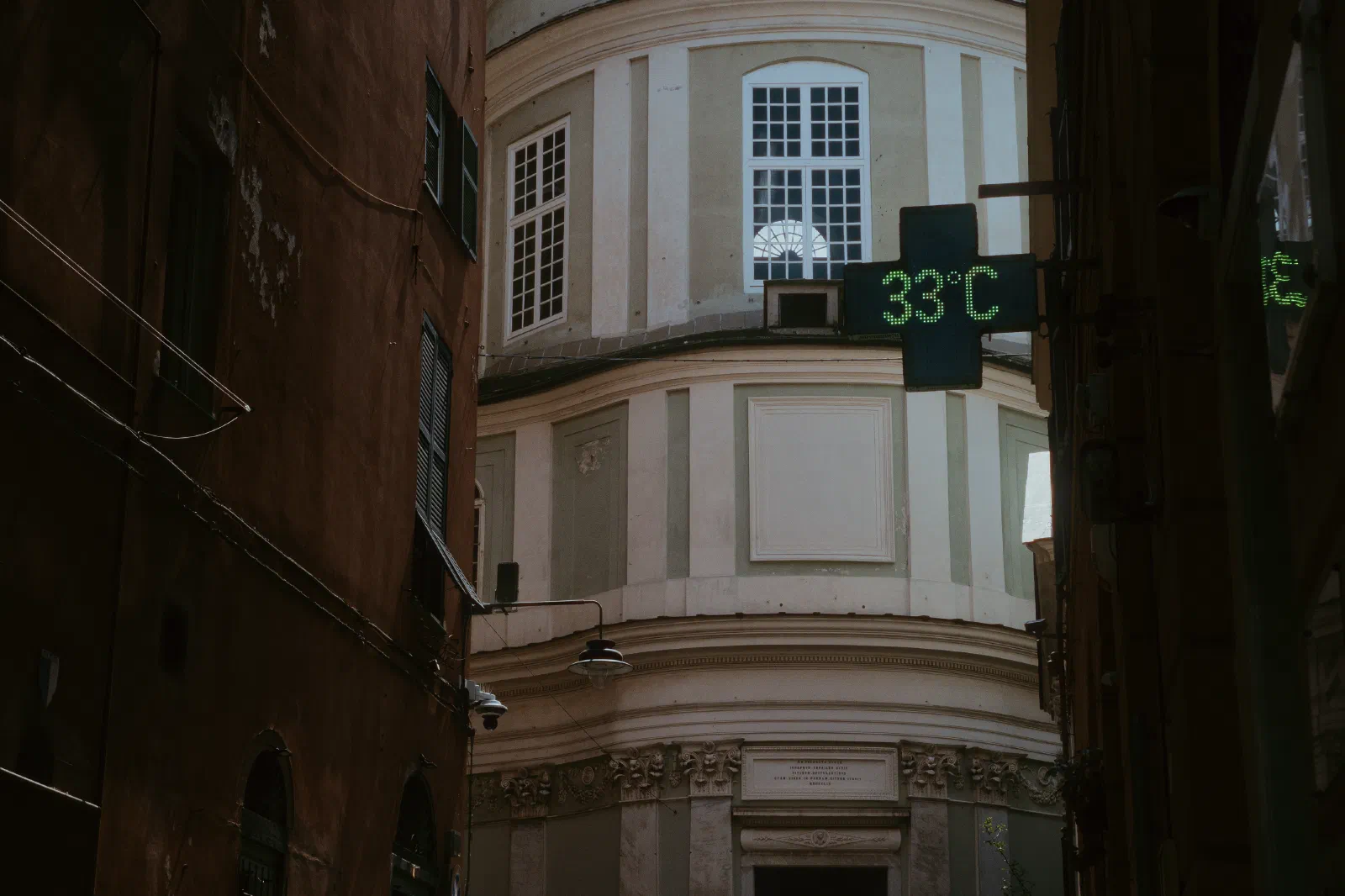 looking down an alleyway in Genoa Italy seeing a church. In the foreground a pharmacy sign reads 33ºC
