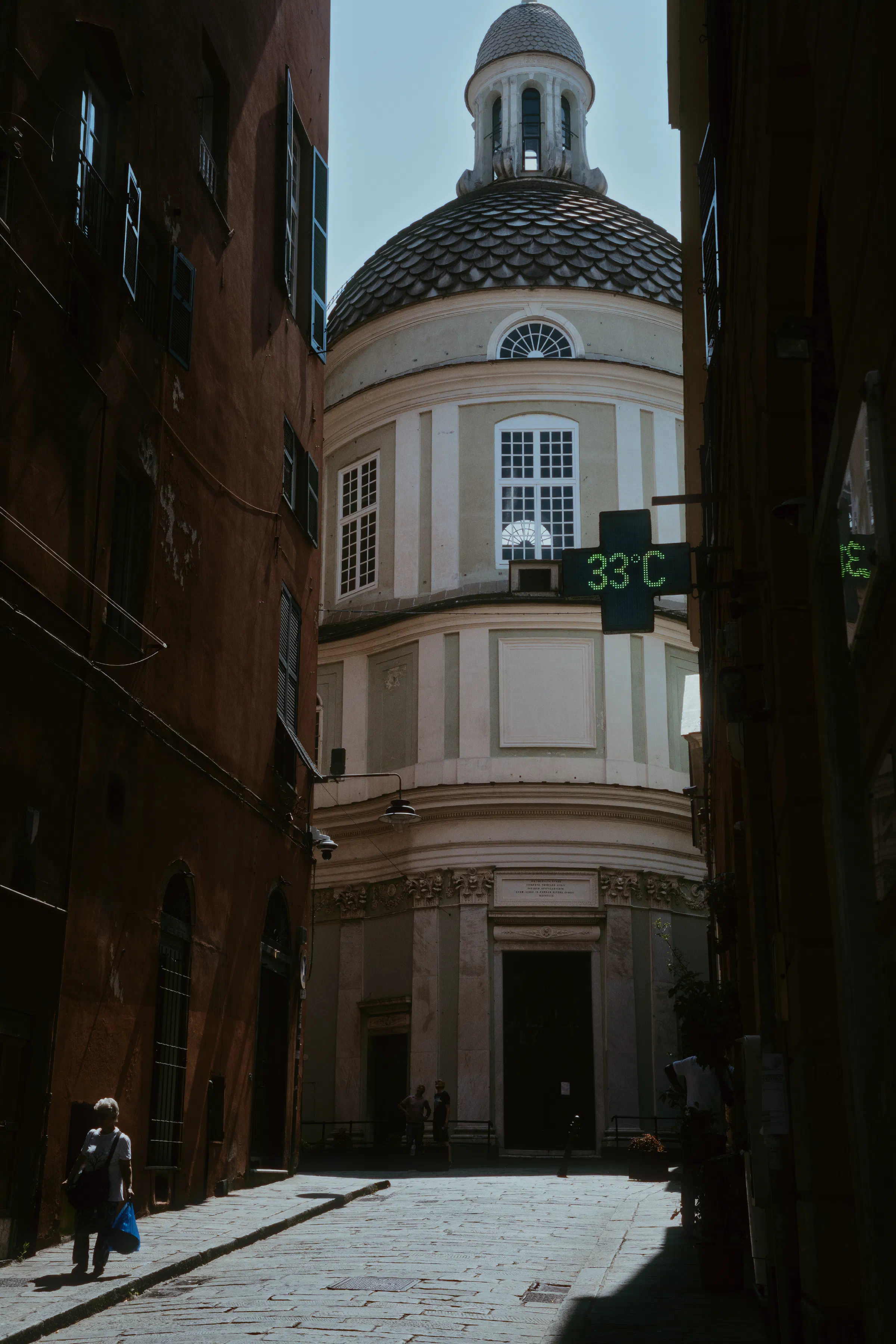 looking down an alleyway in Genoa Italy seeing a church. In the foreground a pharmacy sign reads 33ºC